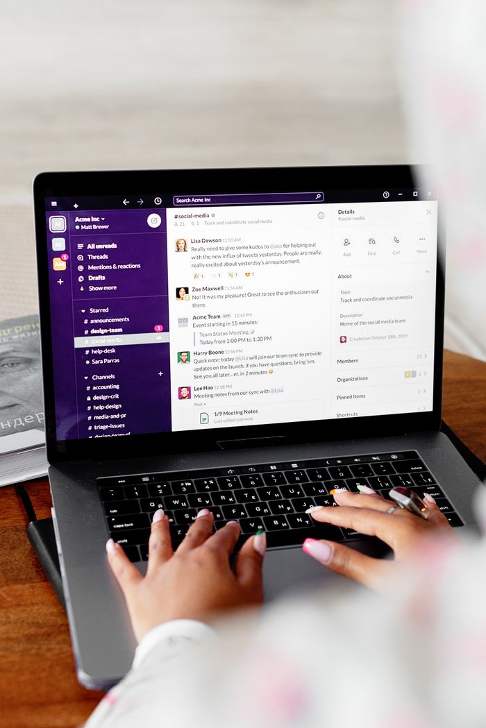 Close-up of hands typing on a laptop displaying Slack for remote communication.